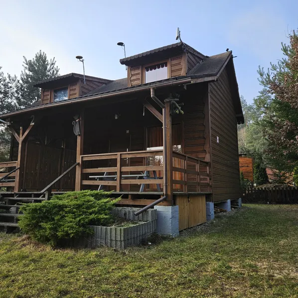 Domek letniskowy (dwupiętrowy) z drewnianą elewacją i tarasem, otoczony zielenią