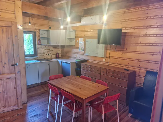 Jasny salon z dużym oknem, szafką, telewizorem, fotelem i stołem jadalnianym